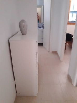 A narrow hallway with a white refrigerator and a vase on top.
