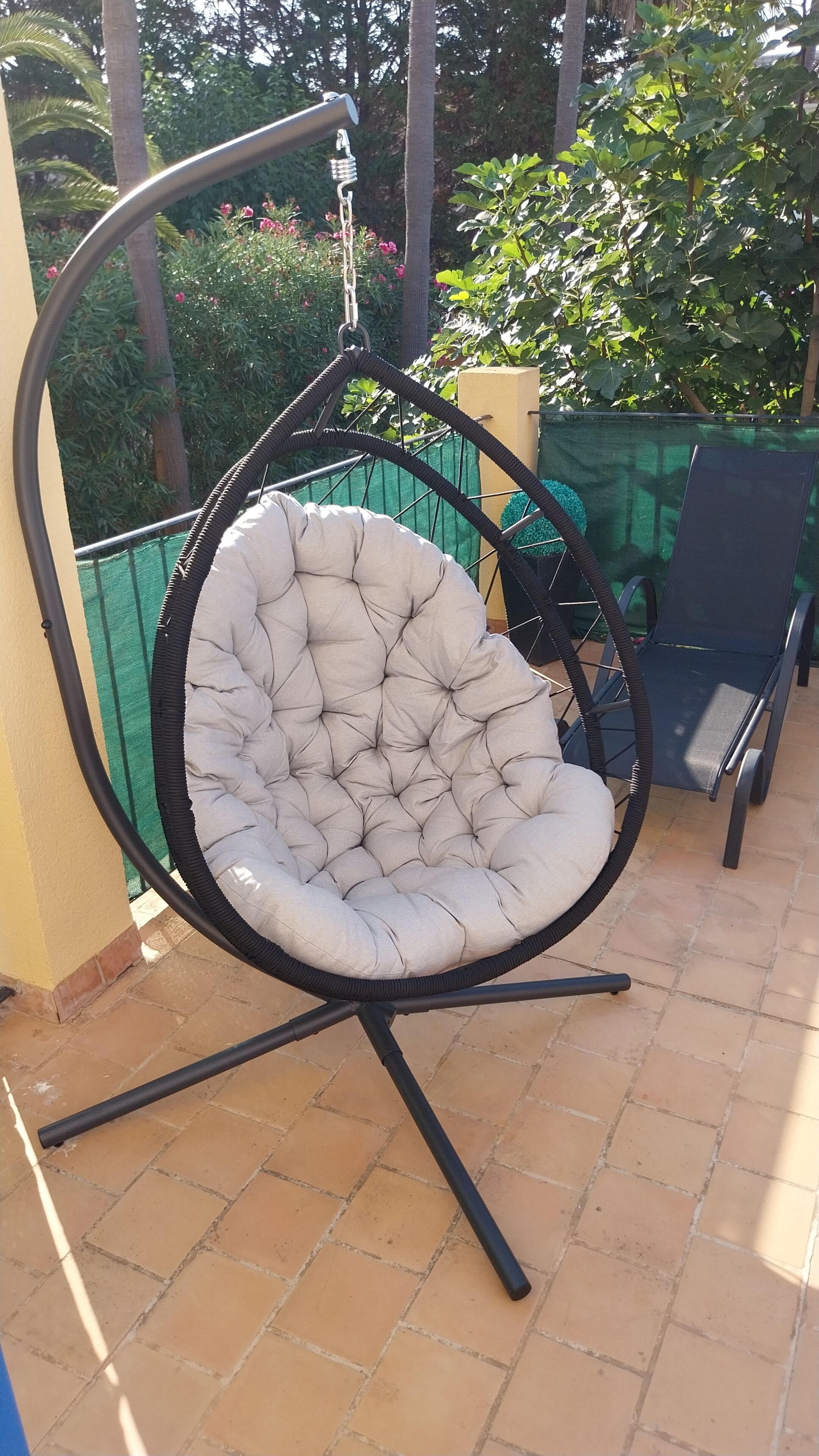A hanging chair with a cushioned seat and back, supported by a metal frame, on a tiled patio.