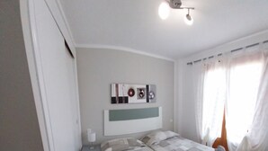Une chambre avec deux lits, une table de chevet, une lampe fixée au mur et un ventilateur de plafond.