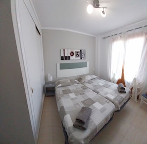 A bedroom with two beds, a nightstand, a wall-mounted lamp, and a ceiling fan.