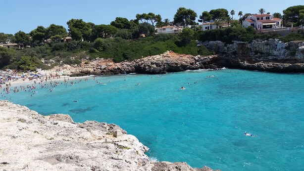 Une zone côtière caractérisée par des eaux turquoise et limpides, des falaises rocheuses et une plage animée.