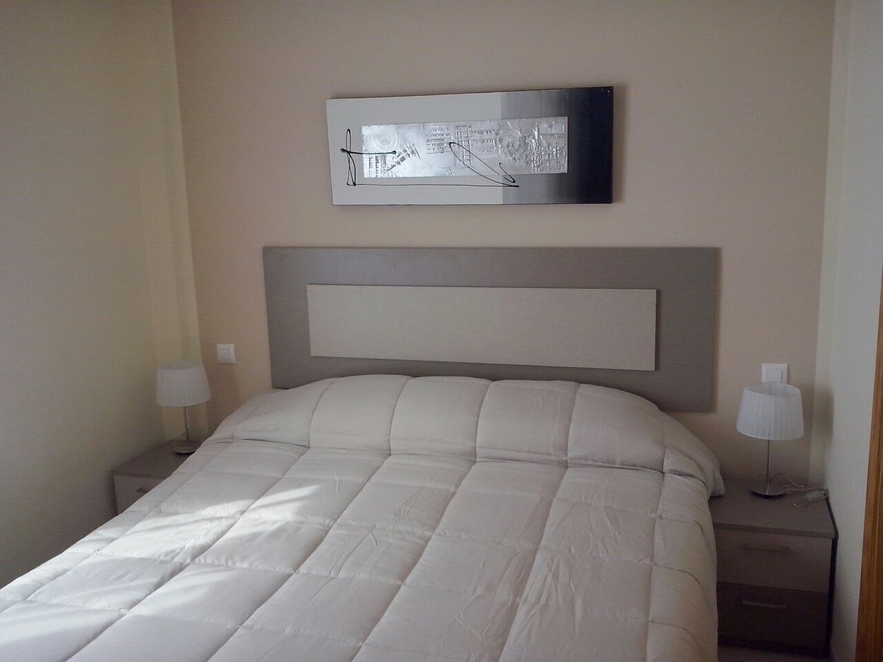 A neatly made bed with a headboard, two bedside tables with lamps, and a framed picture on the wall.