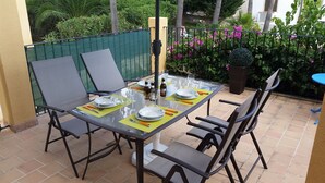 Un espace de restauration en plein air avec une table en verre prévue pour quatre personnes, entourée de chaises.