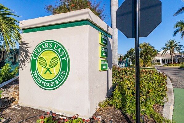 A sign for Cedars East Tennis Resort & Club with directional arrows to the clubhouse, restaurant, and rental office. - Peaceful Condo – Cedars East #803 by RVA (Longboat Key)