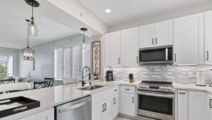 A modern kitchen with white cabinets, stainless steel appliances, and a striped rug. - Peaceful Condo – Cedars East #803 by RVA (Longboat Key)