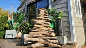 A house with a wooden staircase leading to the entrance, surrounded by potted plants and a deck. - West Seattle Driftwood Cottage - Firepit + Walk to Coffee & Restaurants (Seattle)