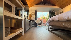 A compact room with a bed, a kitchenette, a dining area, and a view of the outdoors. - West Seattle Driftwood Cottage - Firepit + Walk to Coffee & Restaurants (Seattle)
