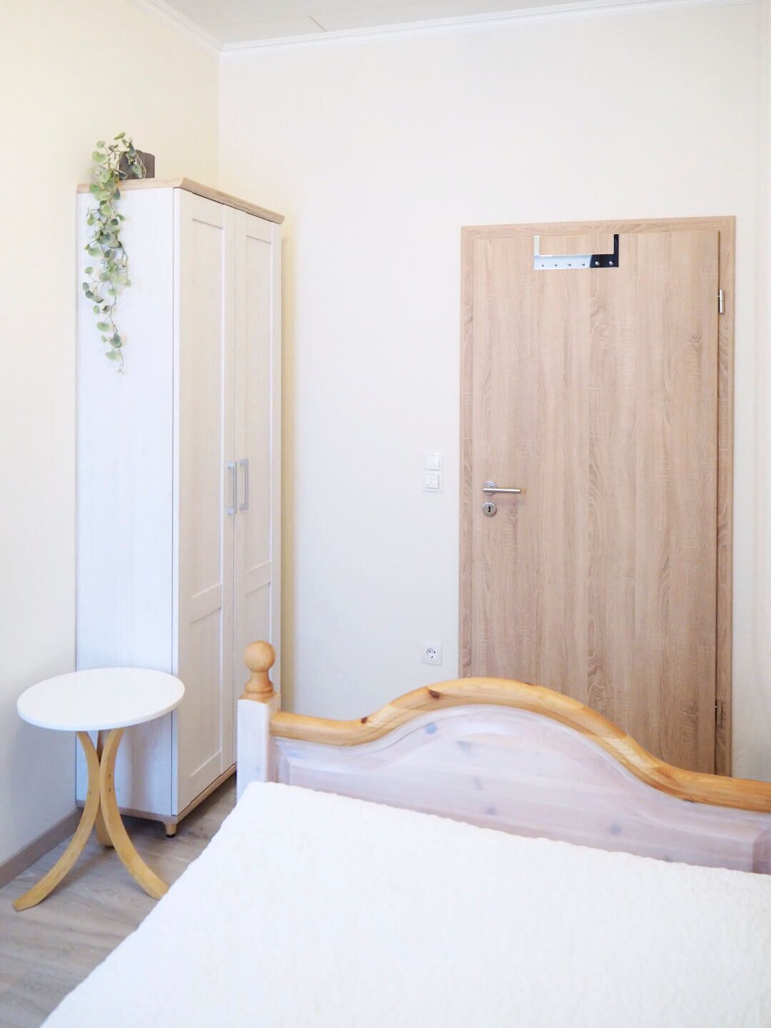 A bedroom with a bed, a wardrobe, a small round table, and a wooden door.