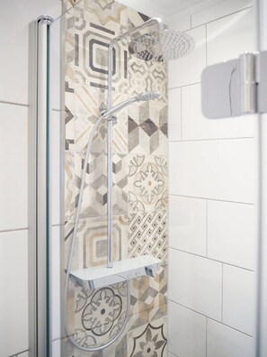 Ducha con salpicadero de azulejos geométricos y cabezal de ducha cromado.