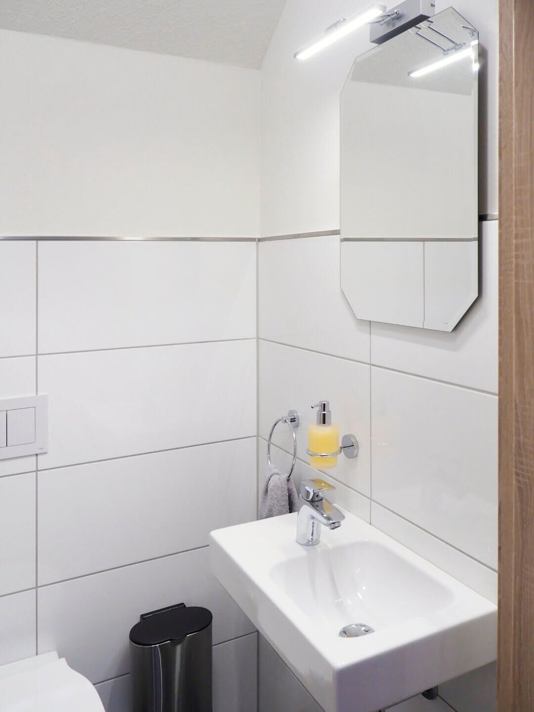 Een moderne badkamer met een witte wastafel, spiegel en betegelde wanden.