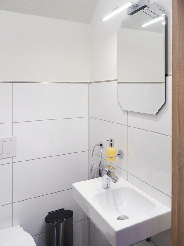 Une salle de bain moderne avec un lavabo blanc, un miroir et des murs carrelés.