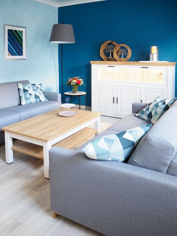 Una sala de estar moderna con un sofá gris, una mesa de centro de madera y un mueble blanco con puerta de cristal.