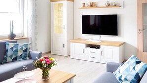 Una sala moderna con un sofá, una mesa de centro con un jarrón de flores, un televisor sobre un mueble de madera y un aparador con puertas de cristal.
