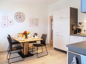 Una cocina moderna con armarios blancos, una mesa de comedor de madera con sillas negras, un reloj y cuadros en la pared.