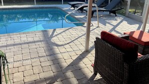 Zona de piscina amb una piscina blava cristal·lina, gandules i un porxo cobert amb sòl de rajoles.