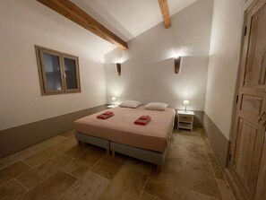 Une chambre à coucher avec un lit, deux tables de chevet avec des lampes, une fenêtre et une porte en bois.