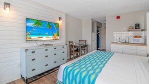 A bedroom with a bed, a TV on the wall, a desk, and a kitchenette. - Landmark 607 (Myrtle Beach)