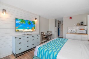 Un dormitorio con cama, televisión en la pared, escritorio y kitchenette.