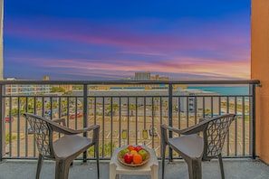 A balcony with two chairs and a table with fruit, overlooking a parking lot and buildings. - Landmark 607 (Myrtle Beach)