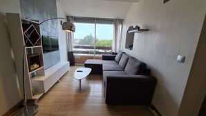 Una sala de estar moderna con un sofá seccional, un televisor de pantalla plana, una mesa de centro y un amplio ventanal con vistas al exterior.