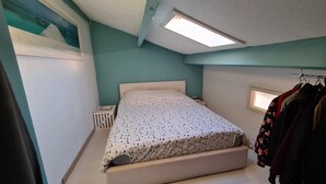Un dormitorio con cama, mesita de noche, armario y tragaluz.