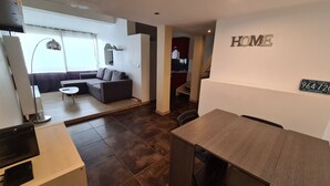 Una sala moderna con un sofá modular, una mesa de comedor y una cocina al fondo.