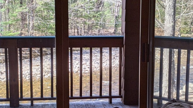 A wooden deck with a view of a rocky stream and trees.