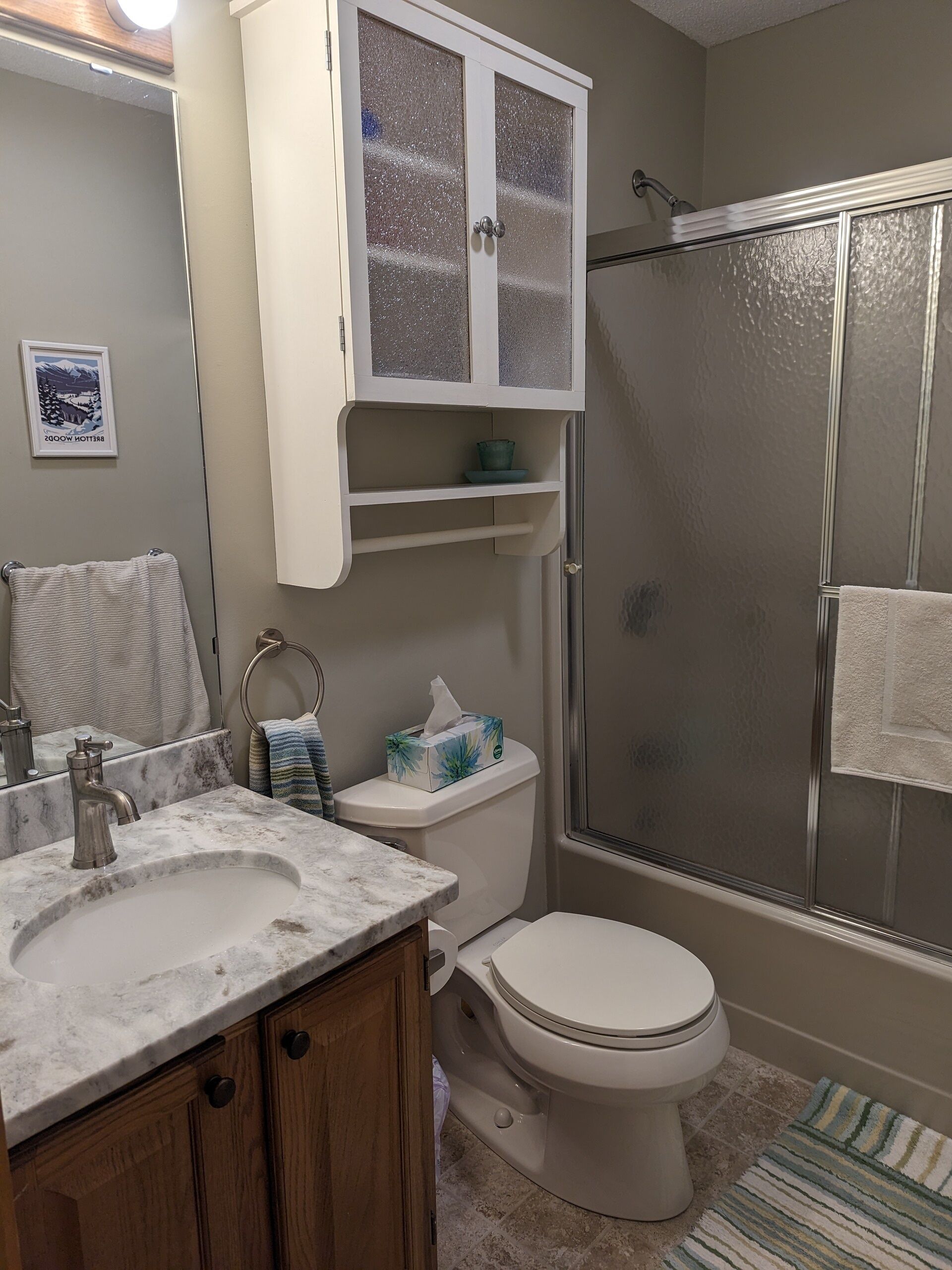 Une salle de bain avec un lavabo en marbre, des toilettes, un espace douche et un meuble avec des portes en verre dépoli.