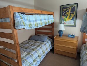 A bunk bed with a plaid bedspread, a bedside table with a lamp, and a framed picture on the wall.