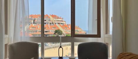Una habitación con dos sillones mirando hacia una ventana grande con vistas a una playa y edificios.