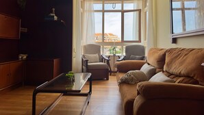 Una sala de estar acogedora con un sofá, un sillón y una mesa de centro, una estantería y un ventanal con vistas.