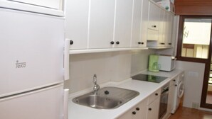 A compact kitchen with white cabinets, a stainless steel sink, a microwave, and a washing machine.