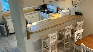 A modern kitchen with a wooden island, white chairs, and a dining table. - Amelia Island oceanfront home on Sandpiper Loop, amazing views & steps to ocean (Fernandina Beach)
