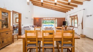 Un espace repas avec une table et des chaises en bois, un plafond en bois avec des poutres apparentes et une vue sur l’extérieur par une fenêtre.