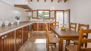 Une cuisine avec des meubles en bois, un îlot central, une table à manger avec des chaises et une fenêtre donnant sur un espace verdoyant.