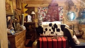 A cozy room with a cowhide-covered armchair, a red blanket, and a vintage mirror. - CARRIAGE HOUSE (Monticello)