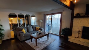 A living room with a sofa, coffee table, and a large plant. There is a fireplace and a view of a body of water through the windows. - Best Pricing on the Main Channel at the Lake! (Osage Beach)