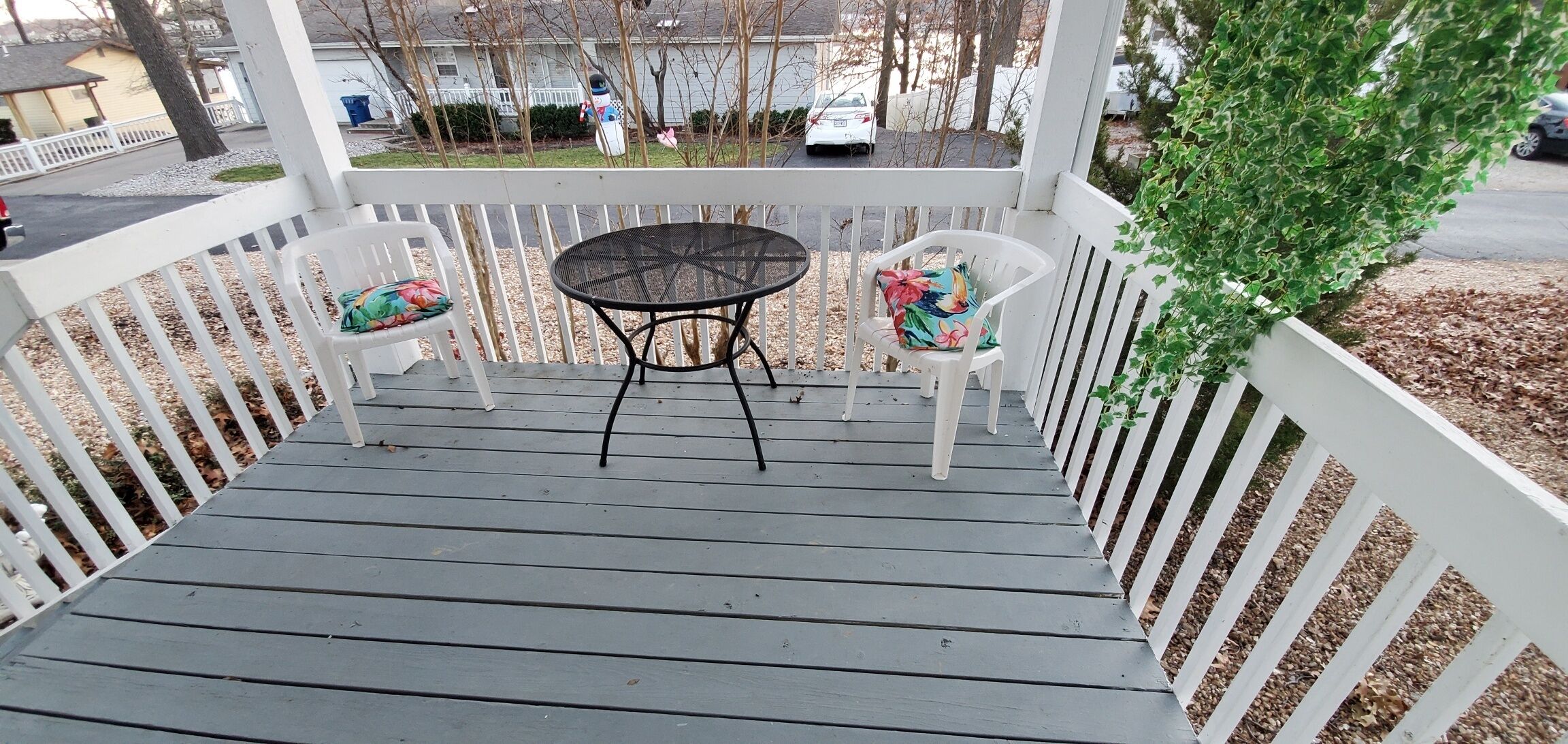A covered porch with a table and two chairs, surrounded by a white railing.