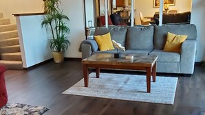 A modern living room with a dark wood floor, a grey sofa with yellow cushions, a wooden coffee table, and a large mirror above the sofa. - Best Pricing on the Main Channel at the Lake! (Osage Beach)