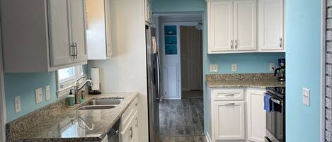 A kitchen with white cabinets, a granite countertop, and a wooden floor.