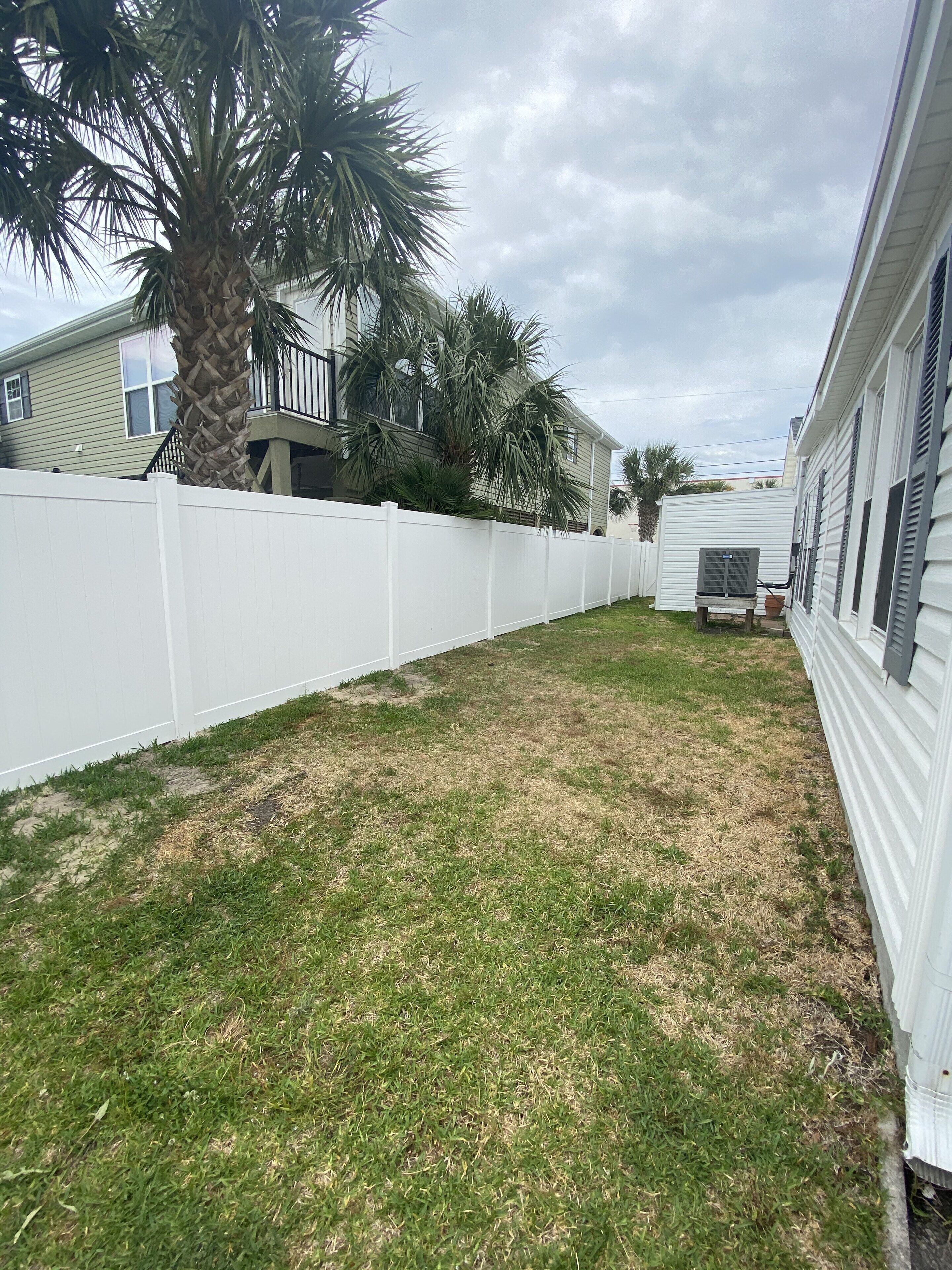 A residential area with a white fence, a grassy yard, and a mobile home.