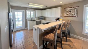 A kitchen with white cabinets, a microwave, and a bar area with wicker chairs. - Seaport Village 1457 - Second Row in Garden City Beach (Garden City Beach)