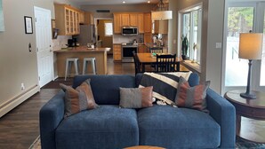 Una cocina moderna con armarios de madera, un comedor con mesa y sillas, y una sala de estar con sofá y lámpara.