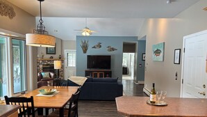 Una cocina moderna con comedor, una sala de estar con sofá y televisor, y un pasillo que conduce a otra habitación.