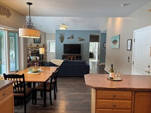 A modern kitchen with a dining area, a living room with a sofa and TV, and a hallway leading to another room.
