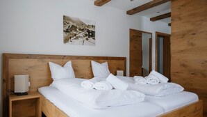 Una cama bien hecha con sábanas y toallas blancas, una lámpara de noche y un cuadro en la pared.