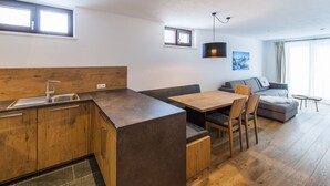 Una cocina moderna con encimera de madera y armarios empotrados, un comedor con mesa y sillas, y una sala de estar con sofá y un cuadro.