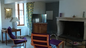 A living room with two rocking chairs, a television, a fireplace, and a small table with a lamp. - Maison de Village Agréable à Vivre (Précy-le-Sec)