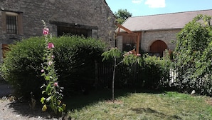 A stone building with a sloped roof, a gravel driveway, and a flower bush in the foreground. - Maison de Village Agréable à Vivre (Précy-le-Sec)