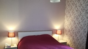 A bedroom with a bed, two bedside lamps, a nightstand, a patterned wall, and a ceiling light. - Maison de Village Agréable à Vivre (Précy-le-Sec)